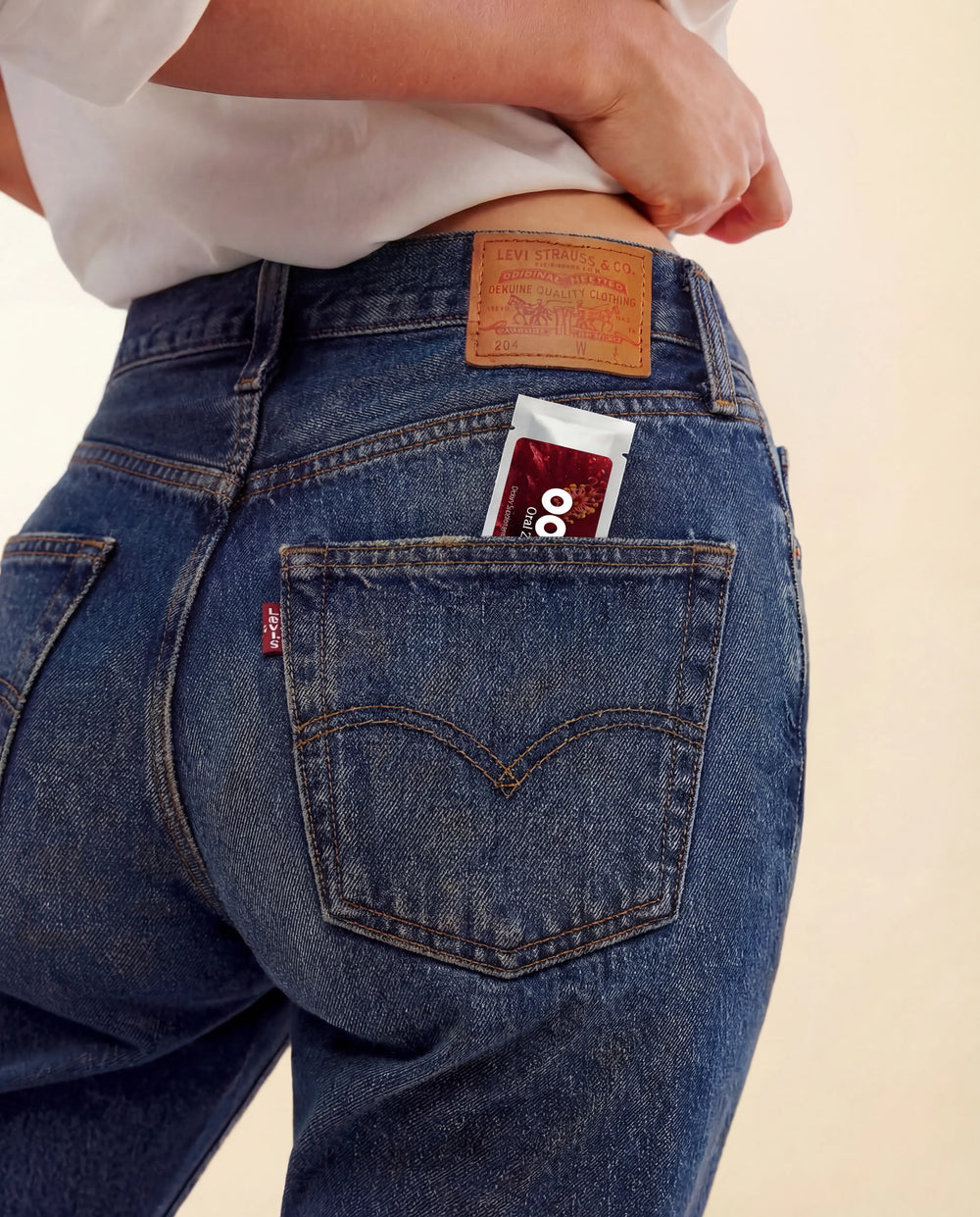 Woman wearing blue jeans with a Levi's logo, showing the back pocket which contains a packet of Oral Zen natural gag reflex control.